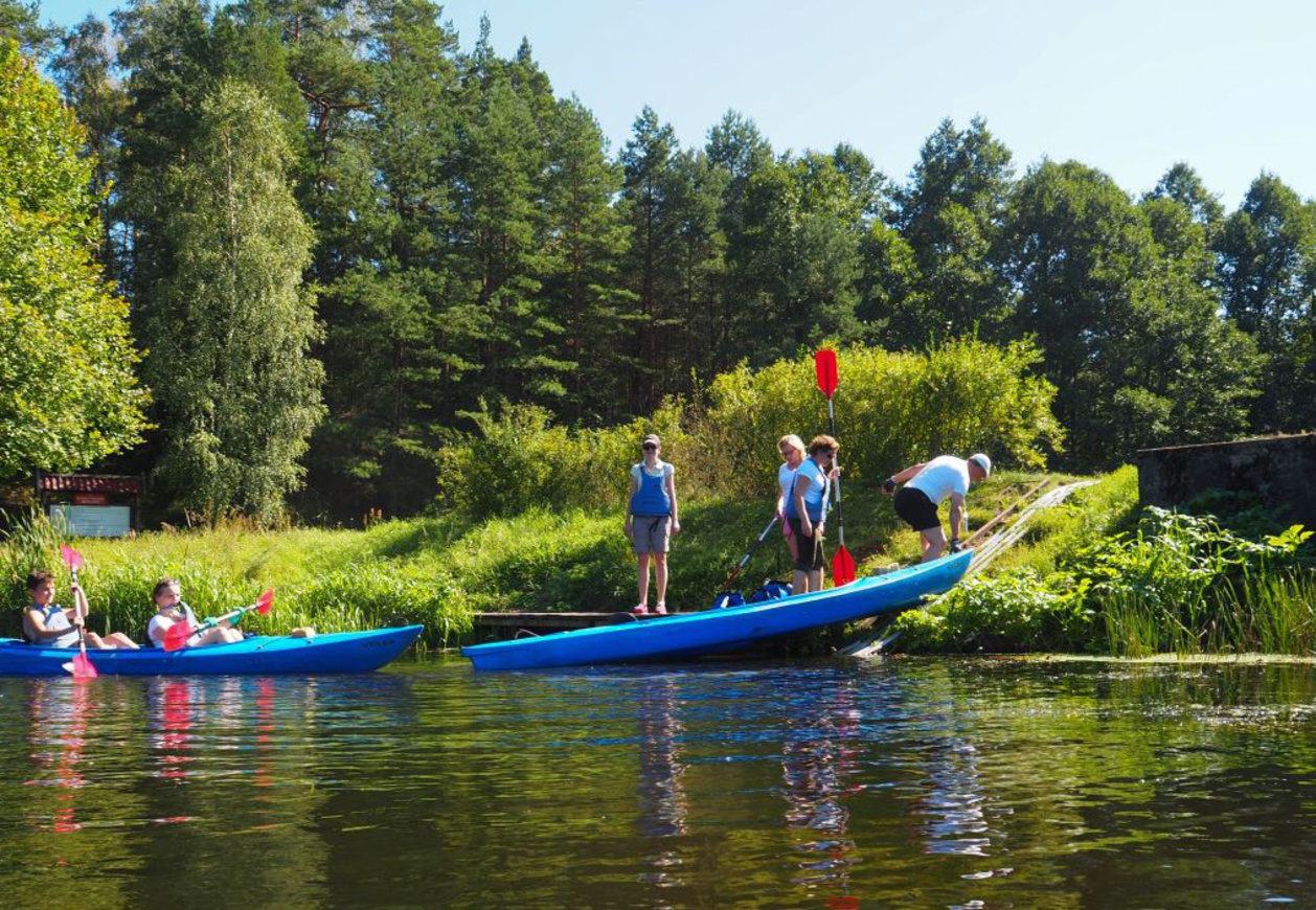Zdjęcie przedstawia kajakarzy szykujących się do wejścia do swoich kajaków.